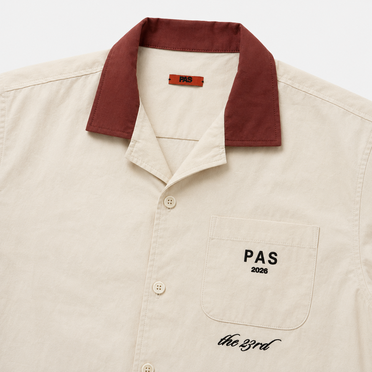 PAS The 23rd One Tribe cream button-up shirt – burgundy contrast collar, PAS 2026 pocket embroidery, Be One Tribe Unite the World crest on back